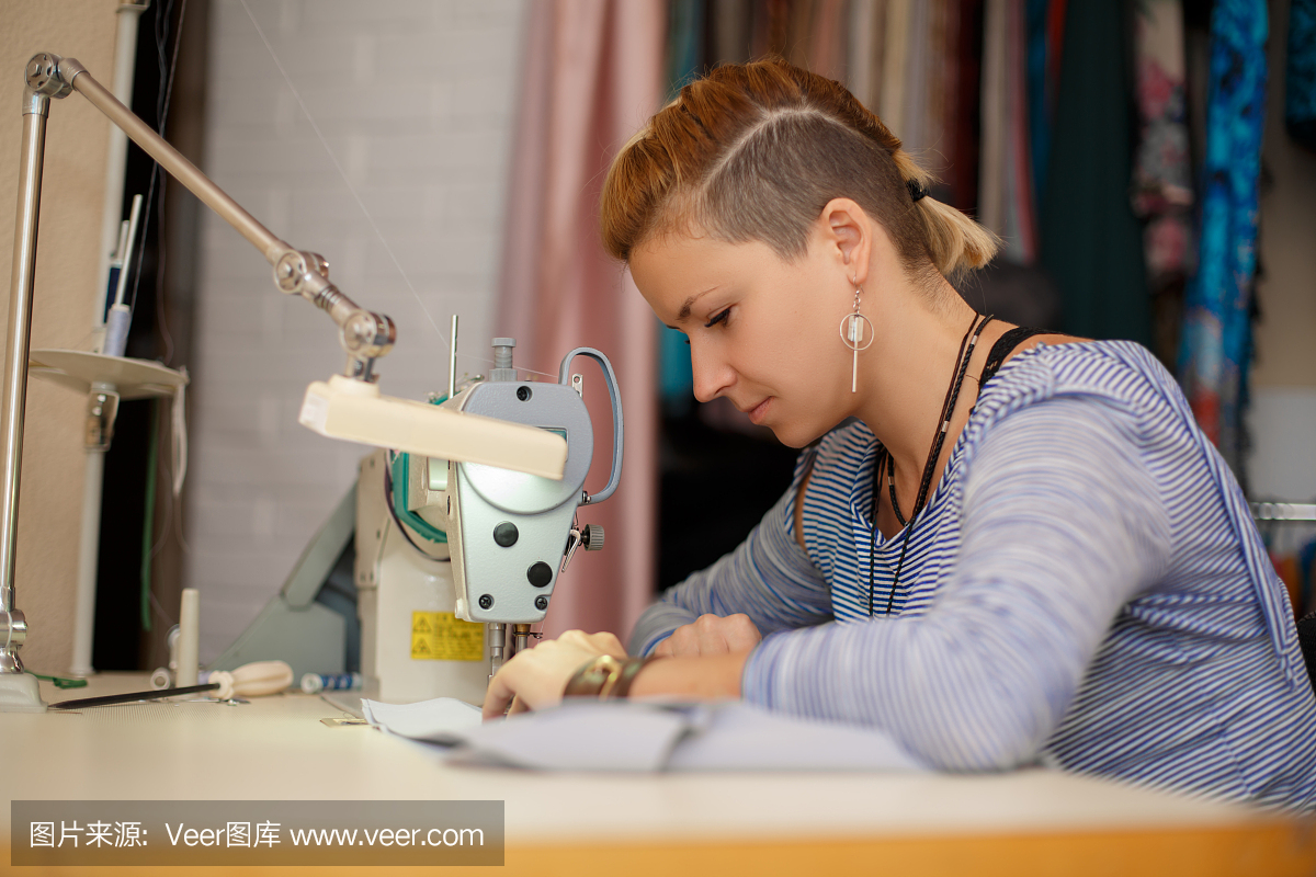 年轻的金发女裁缝在缝纫机上工作。服装制造业。